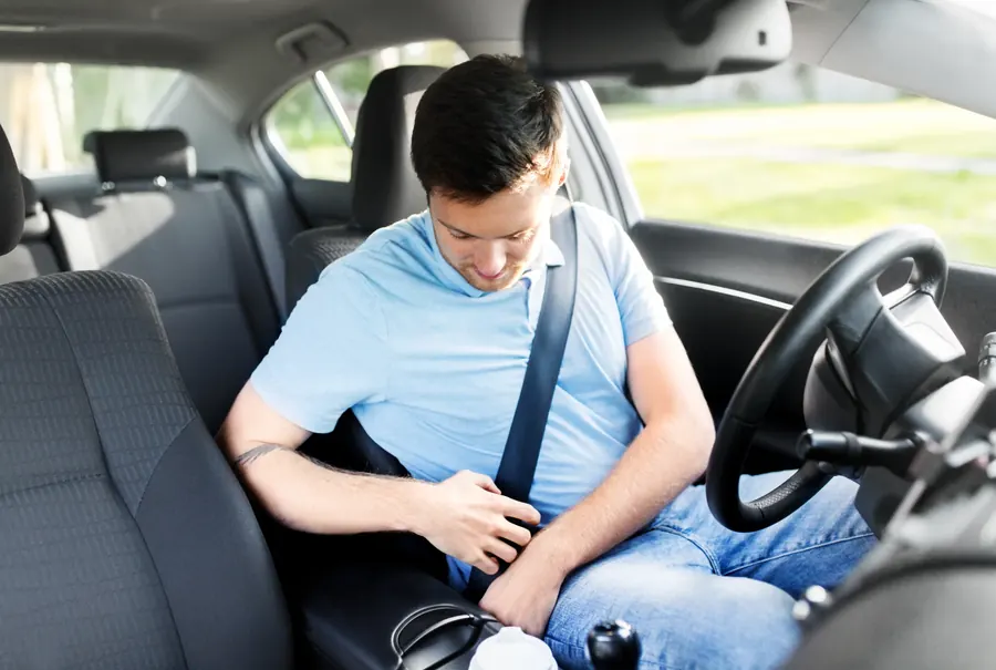 A person fastening a seatbelt in the rear seat of a car, seen from the front of the cabin.