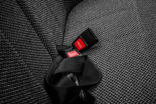 A black seatbelt webbing strap and buckle resting in the crease of a dark vehicle seat.