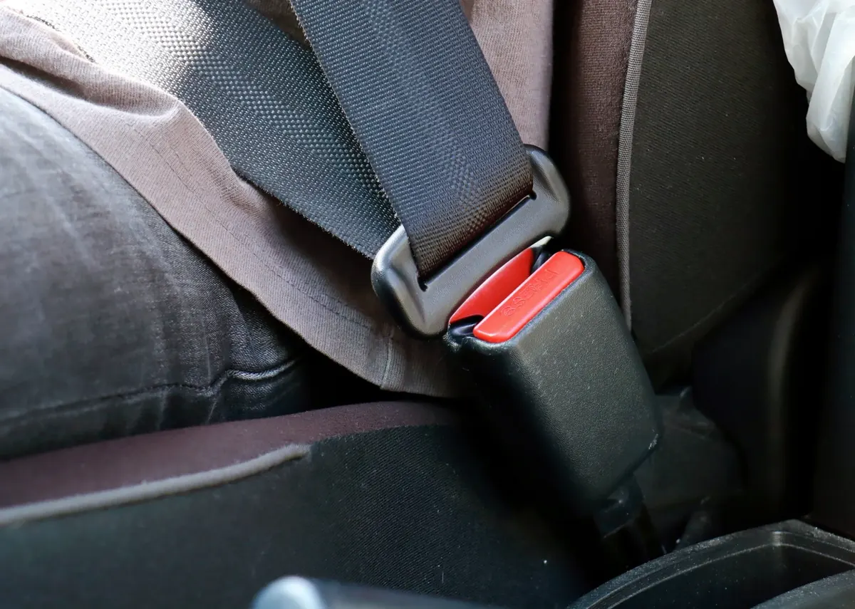 A fastened automotive seatbelt with the latch plate seated in a black buckle receiver on a vehicle seat.