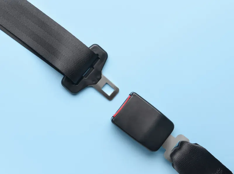A seatbelt latch plate and buckle receiver laid out flat on a pale blue background, separated to show both halves.