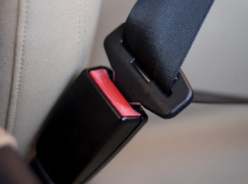 A close view of a seatbelt buckle receiver with its red release button, alongside the webbing and latch plate.