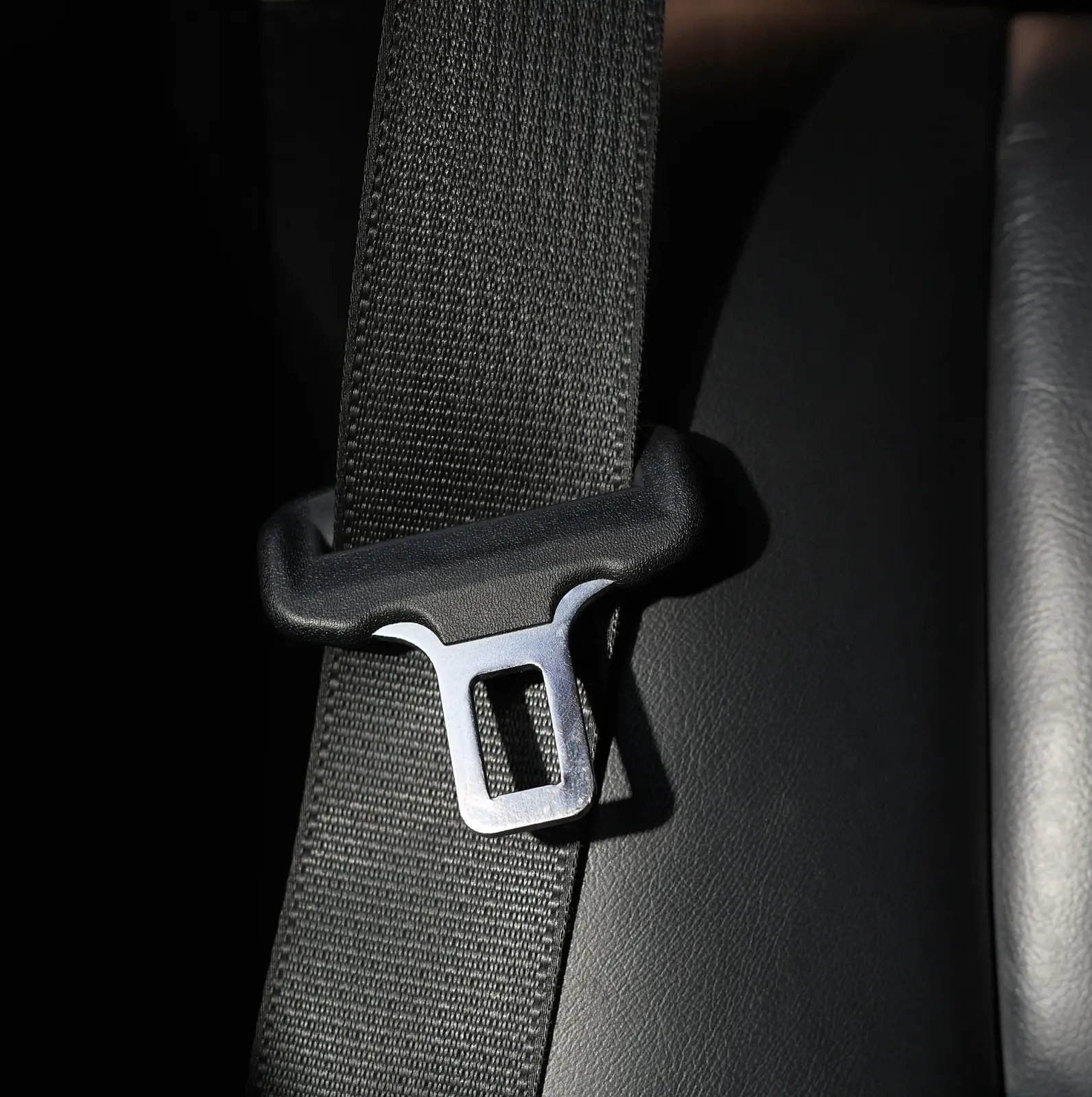 A seatbelt webbing strap running through a moulded guide loop and metal latch plate against a vehicle seat.