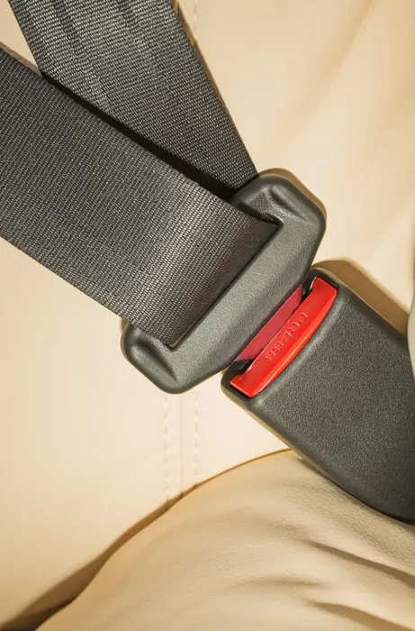 A close view of a grey seatbelt latch plate seated in its buckle receiver against a cream seat, with the red release button visible.