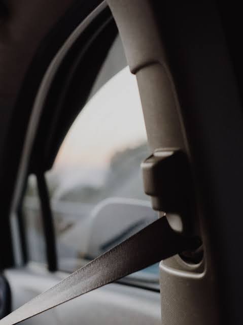 A seatbelt running down the interior pillar of a vehicle past a height adjuster, with the window and door frame behind.